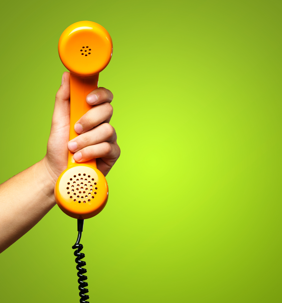 hand holding a corded orange phone against lime green background
